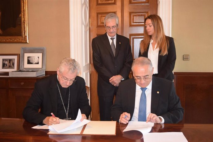 El arzobispo y ministro de Salud, sentados en la mesa, en el momento de firmar el acuerdo