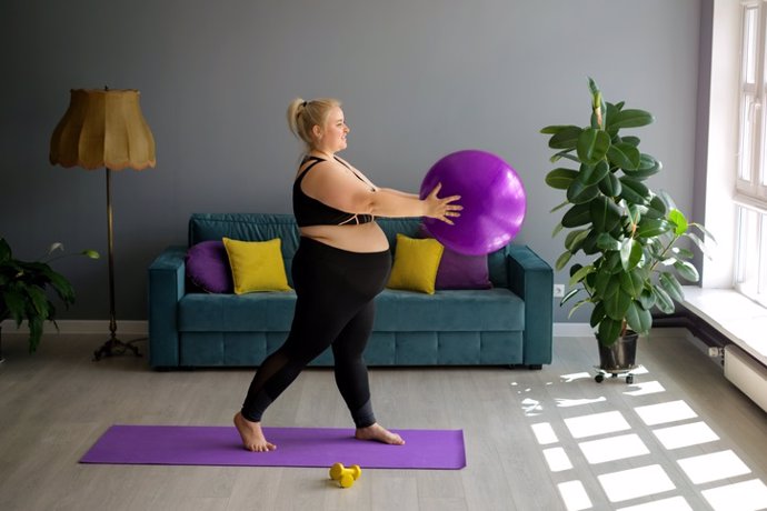Archivo - La mujer embarazada está haciendo Pilates en casa, levantando una pelota en forma sobre sí misma.