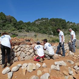 Varias personas construyen un 'marge' aplicando la técnica de la piedra en seco.