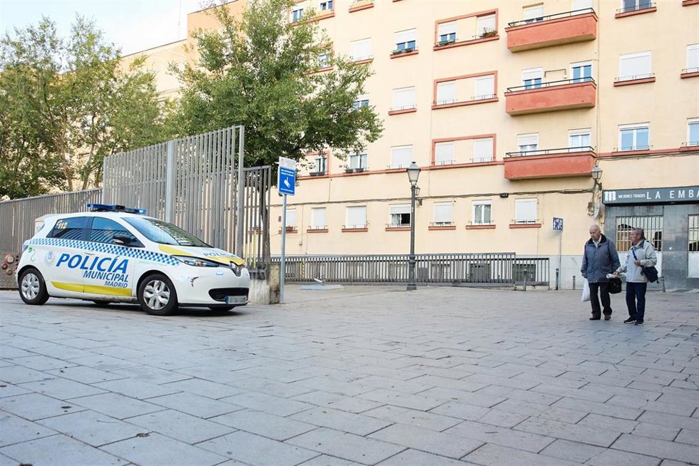 Dos personas mayores pasan junto a un coche de policía municipal a la entrada del parque Casino de la Reina 