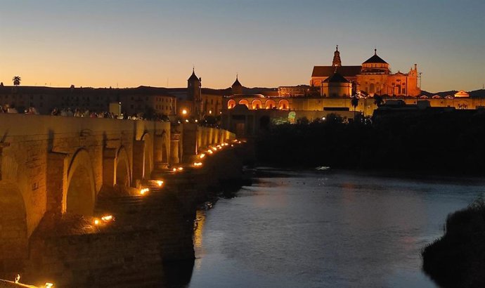 Turistas cruzan el Guadalquivir por el Puente Romano de Córdoba, con la Puerta del Puente y la Mezquita-Catedral al fondo.