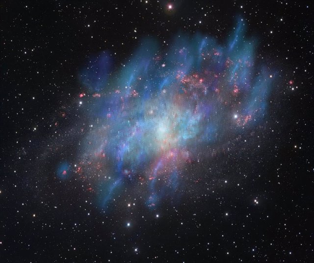 Ilustración artística de vientos impulsados por rayos cósmicos (azul y verde) superpuestos a una imagen en luz visible de la galaxia Triangulum M33 (roja y blanca) observada con el VLT Survey Telescope en el Observatorio Paranal de ESO en Chile.