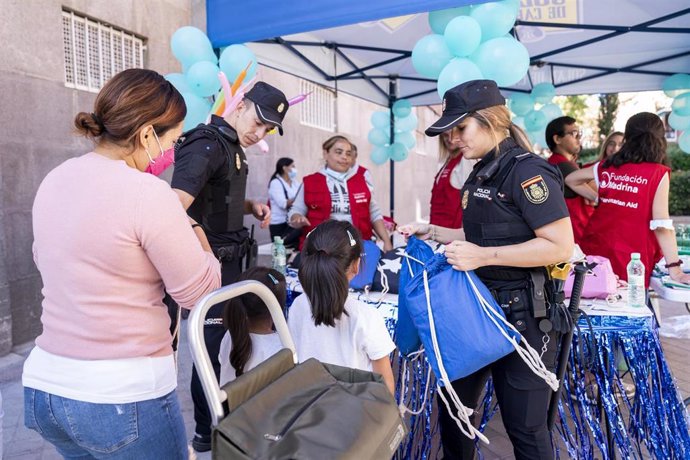 Dos agentes colaboran con la Fundación Madrina en la entrega de un kit completo de material escolar a los niños, en la Plaza de San Amaro, a 27 de septiembre de 2022, en Madrid (España). 