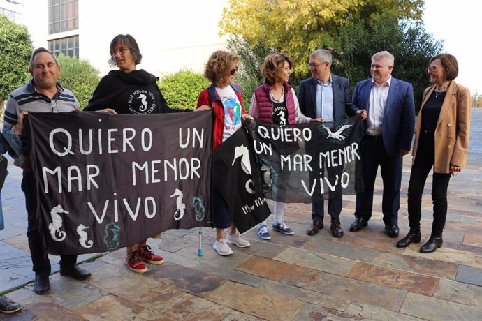 El secretario de Estado de Medio Ambiente, Hugo Morán, y el delegado del Gobierno en la Región, José Vélez, junto a vecinos y vecinas que portan pancartas donde se puede leer 'Quiero un Mar Menor vivo'