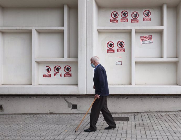 Un hombre mayor con mascarilla y bastón camina delante del Centro de Salud Pavones