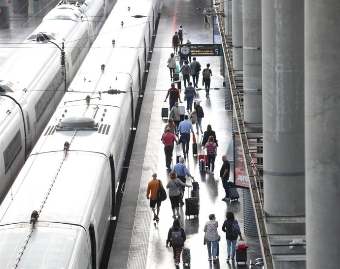 Varios pasajeros con maletas en el andén de un tren