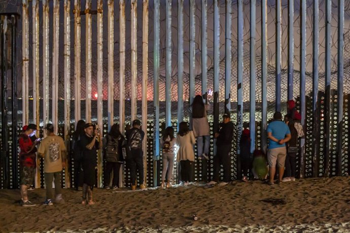 Archivo - Migrantes en la valla que separa México de Estados Unidos en Tijuana