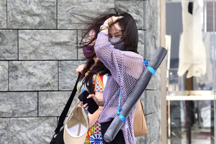 18 October 2022, China, Hong Kong: A woman gestures fixes her hair in the midst of strong wind as unseasonal tropical storm NESAT makes landfall. Photo: Liau Chung-Ren/ZUMA Press Wire/dpa