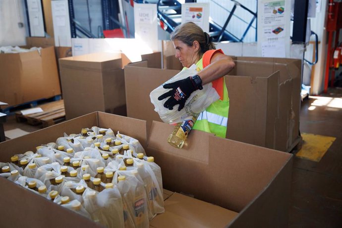 Archivo - Una empleada sostiene una bolsa de botellas de aceite en un banco de alimentos.