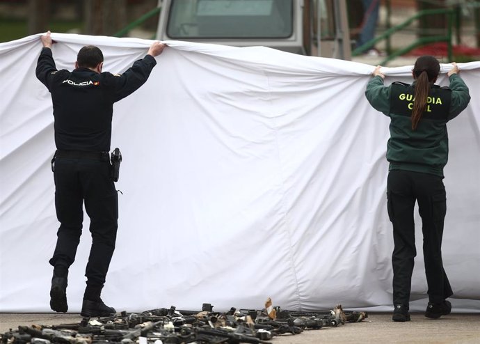 Archivo - Un policía nacional y una guardia civil levantan una sábana para descubrir varias armas durante un acto de destrucción simbólica de casi 1.400 armas, en el Colegio de Guardias Jóvenes Duque de Ahumada, en Valdemoro, Madrid (España), a 4 de mar