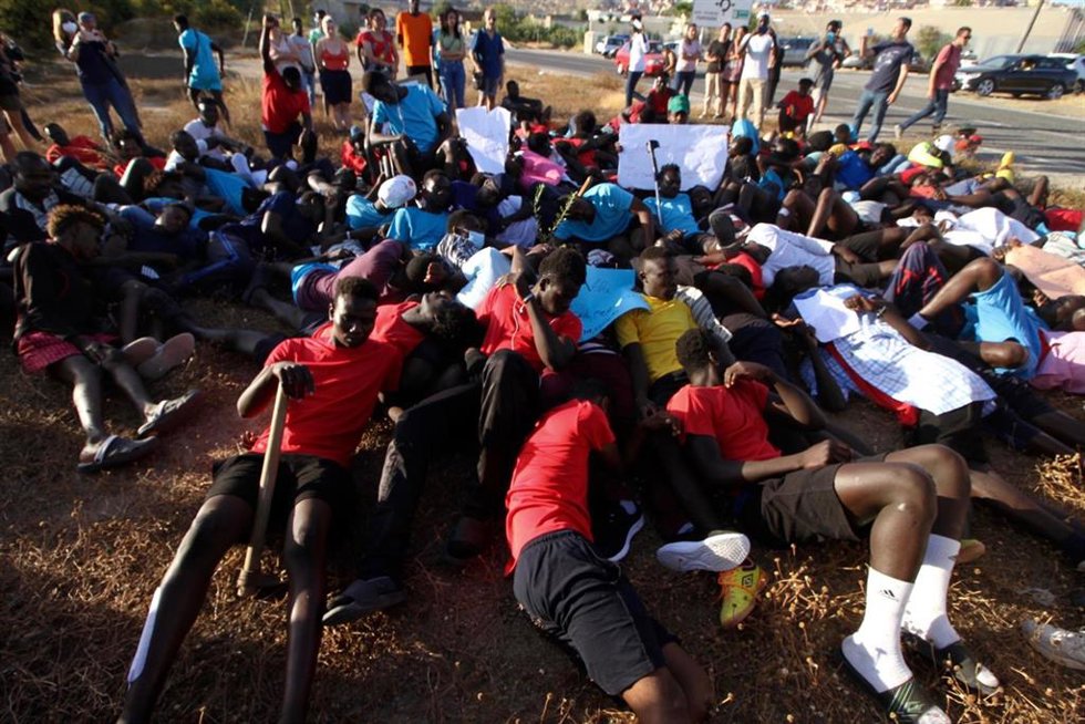 Archivo - Varias personas migrantes tiradas en el suelo simulan las imágenes de los cuerpos tendidos en el salto a la valla de Melilla