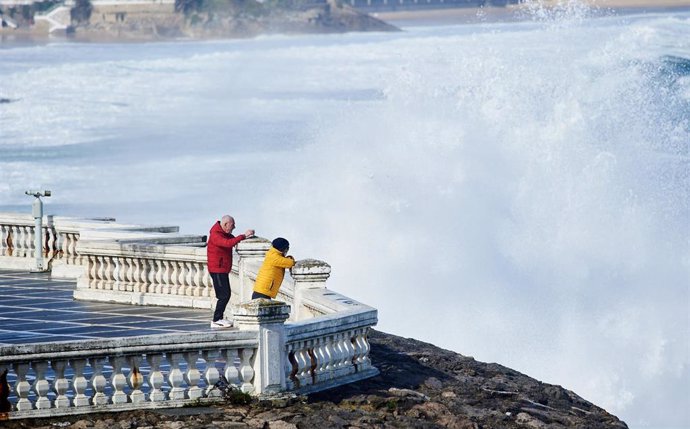 Archivo - Dos personas se hacen una fotografía con el fuerte oleaje, que se aproxima al paseo marítimo,, en Santander.