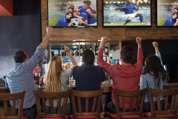 Archivo - Aficionados viendo un partido de fútbol en las pantallas de televisión de un bar