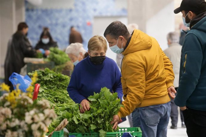 Archivo - Un hombre compra verduras a una vendedora local de verduras y productos del campo, en el mercado tradicional de la Plaza de Abastos de Lugo, a 22 de marzo de 2022