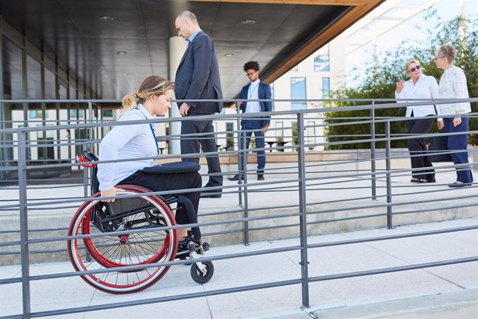 Archivo - Una mujer en silla de ruedas avanza por una rampa de acceso a un edificio.
