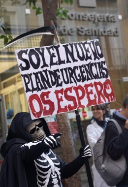 Una persona disfrazada de esqueleto con un cartel en el que se lee: 'Soy el nuevo plan de urgencias, os espero'