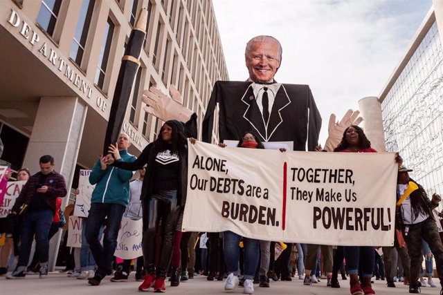 Manifestantes marchan con una pancarta y un cartel de Biden alrededor del Departamento de Educación durante una manifestación para pedir la condonación de deudad universitarias