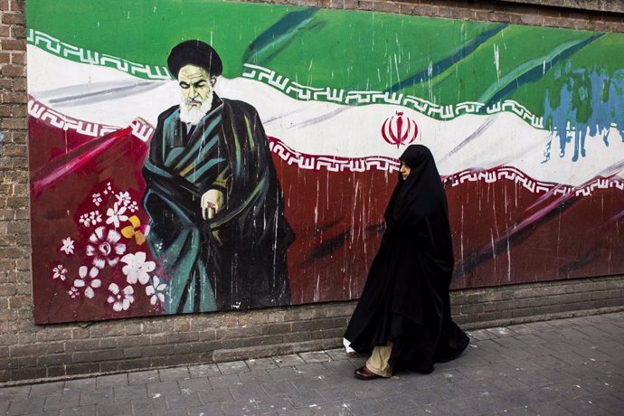 Una mujer junto a un mural con la bandera iraní y el ayatolá Ruholá Jomeini en Teherán