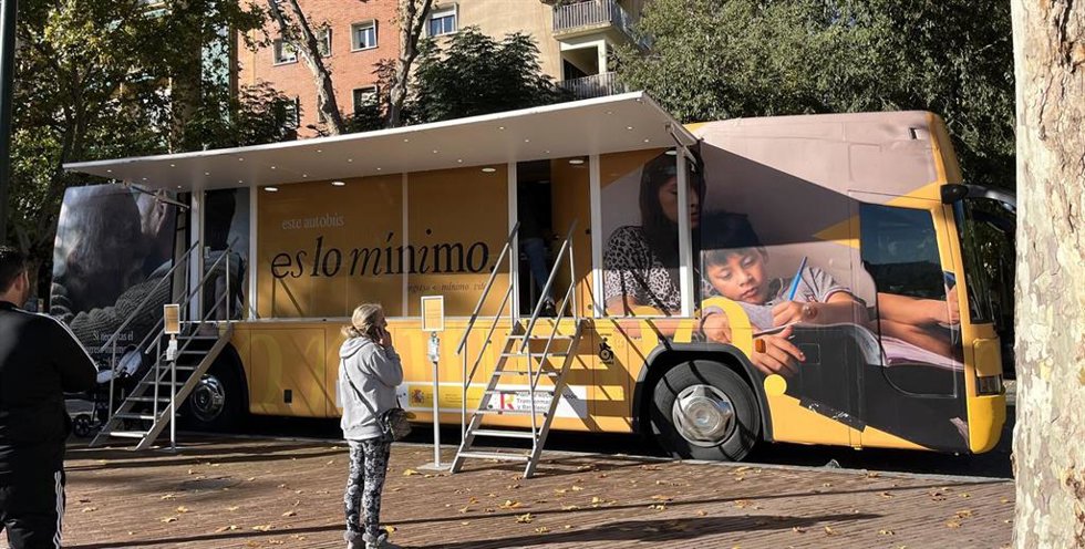 Una mujer habla por teléfono delante del autobús del Ingreso Mínimo Vital