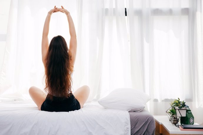 Archivo - Back of young woman sitting and stretching up on bed  MUJER, CAMA, ESTIRAMIENTO, DESPERTARSE