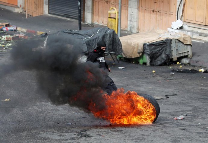 21 October 2022, Palestinian Territories, Hebron: A Palestinian protester push a burn tire during clashes with Israeli forces following a protest after Palestinian Udai Al-Tamimi was killed by Israeli security forces following several days of manhunt. A