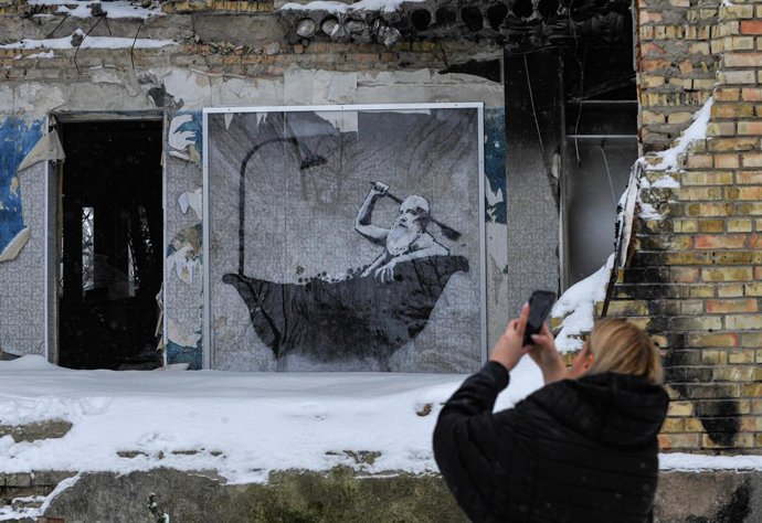 20 November 2022, Ukraine, Gorenka: A woman takes a picture of graffiti by the famous anonymous street artist Banksy which is shown on one of the apartment buildings destroyed by the Russian army in Gorenka. Photo: Sergei Chuzavkov/SOPA Images via ZUMA 