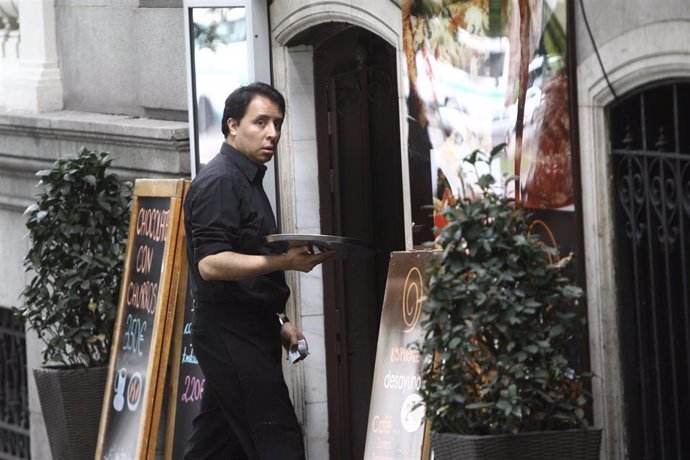 Archivo - Un camarero sostiene una bandeja en la entrada de un bar.