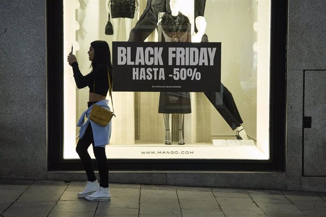 Varias personas pasan por delante de los comercios que anuncian los descuentos del Black Friday, a 23 de noviembre de 2022, en Madrid