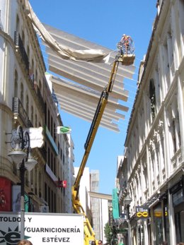 Un operario trabaja en altura colocando toldos en una calle de Córdoba.