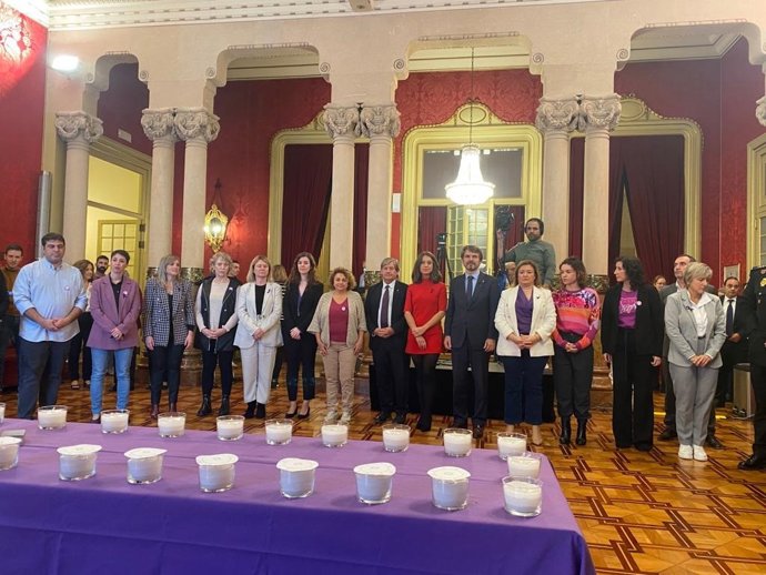 Los portavoces de todos los grupos parlamnetarios, menos Vox, junto a representantes del Parlament y de otras instituciones, al lado de la mesa donde se ha encendido una vela por cada mujer asesinada a mano de su pareja o expareja desde 2003 en España.