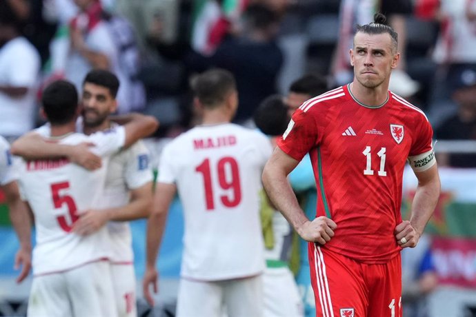 FILED - 25 November 2022, Qatar, Ar-Rayyan: Wales' Gareth Bale looks dejected while Iran players celebrate in the background after the FIFA World Cup Qatar 2022 Group B soccer match between Wales and Iran at Ahmad bin Ali Stadium. Photo: Martin Rickett/
