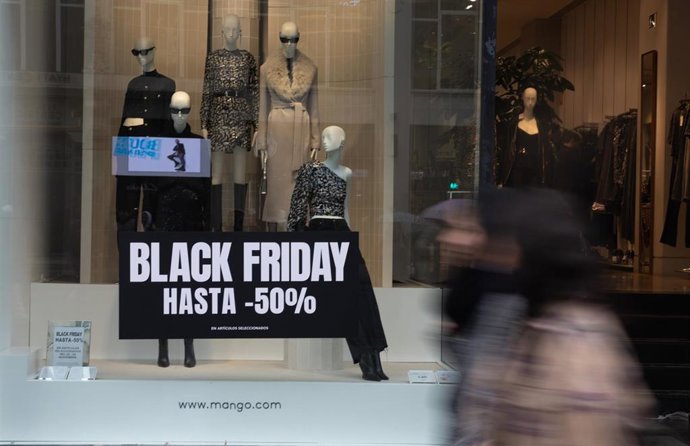 Varias personas pasan por delante de los comercios que anuncian los descuentos del Black Friday.