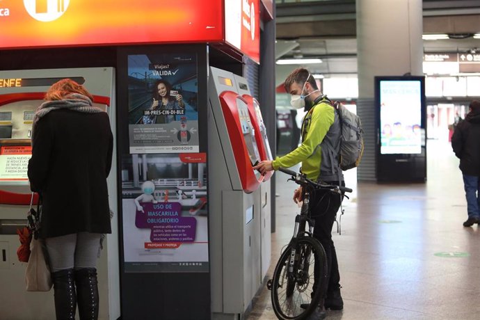 Archivo - Un viajero con bicicleta adquiere un billete en un dispensador en la estación de Atocha 