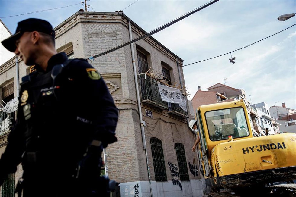Archivo - Un agente de Policía Nacional frente a una máquina retroexcavadora durante la demolición del edificio okupado en Madrid