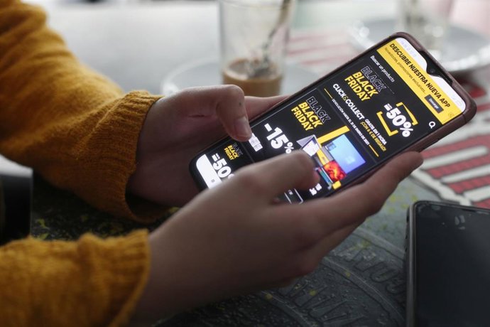 Archivo - Una joven consulta las ofertas de Black Friday de un comercio 