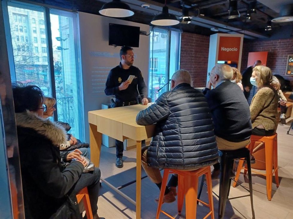 Un agente instruye a personas mayores en el uso seguro de móviles en la tienda de Orange de la calle Tetúan