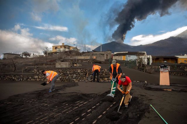 Archivo - Varios voluntarios trabajan retirando cenizas de los tejados de varias casas próximas al volcán de Cumbre Vieja