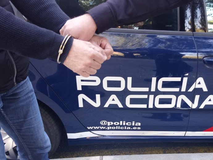 Un varón esposado y conducido por un agente de policía.