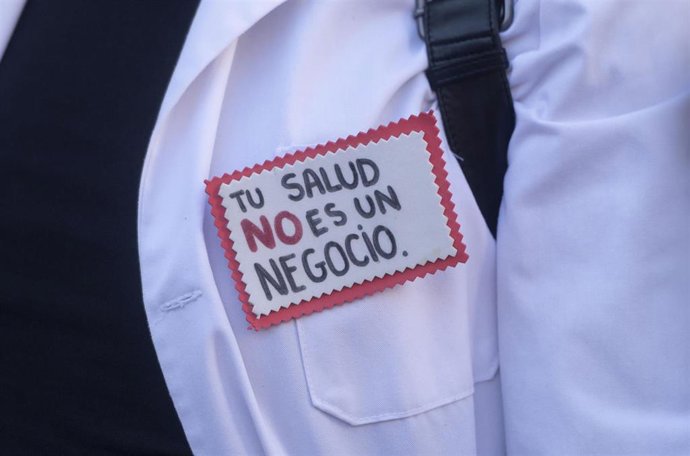 Un hombre con un pin en el que se lee: 'Tu salud no es un negocio'