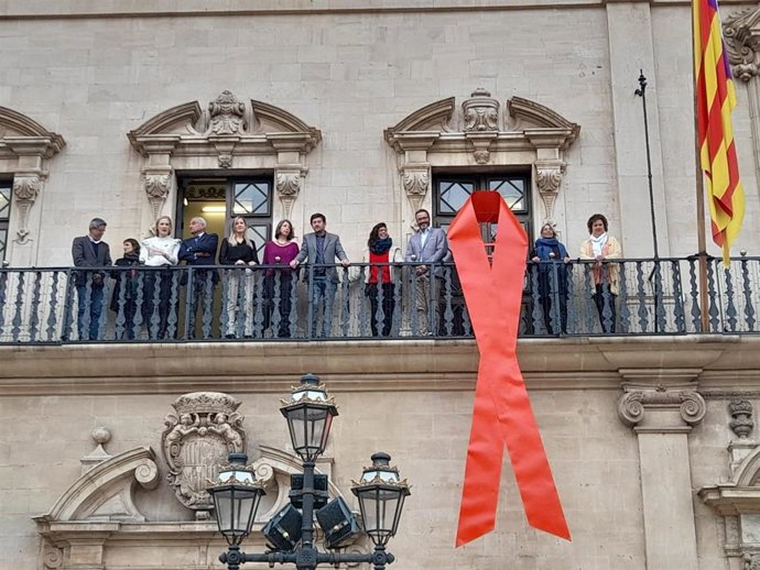 Momento donde se ha colgado el gran lazo rojo en la fachada del Ayuntamiento de Palma con motivo del Día de la Lucha contra el SIDA.