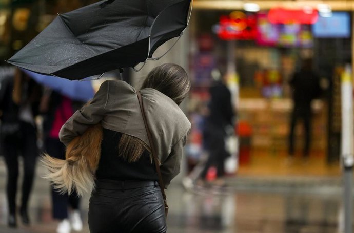 Archivo - Una mujer con un perro intenta controlar y protegerse con un paraguas, en la calle Gran Vía, a 20 de octubre, en Madrid (España). 