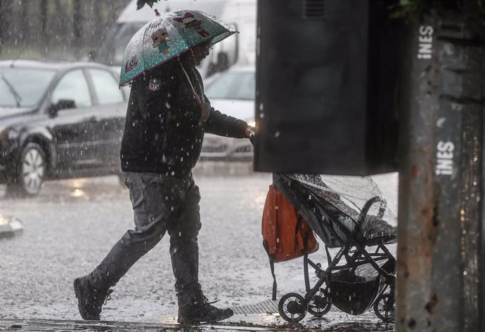 Un hombre lleva un carrito de bebé mientras se protege de la lluvia con un paraguas.