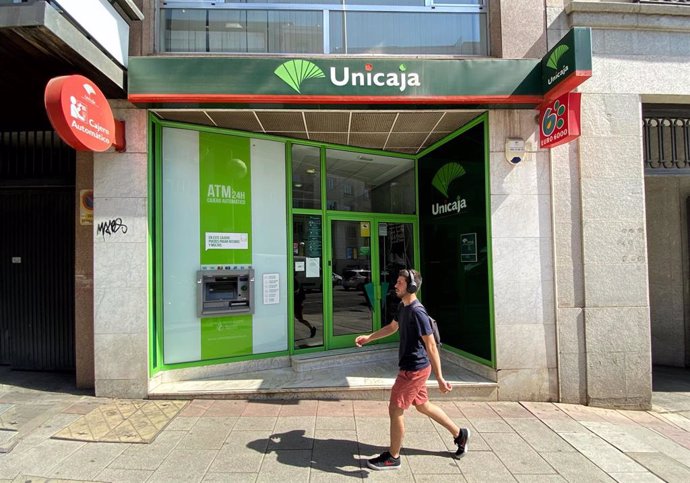 Archivo - Una persona pasa por delante de una oficina de Unicaja.