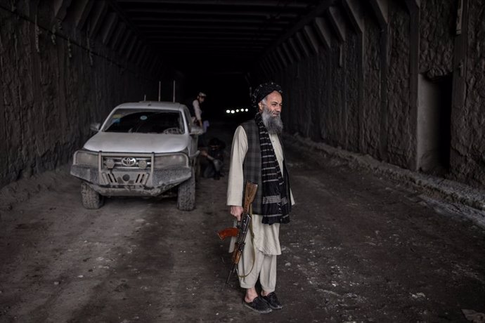 13 November 2022, Afghanistan, Salang Pass: A member of the Taliban, armed with an AK-47 assault rifle, waits as a man mounts tyre chains on his vehicle in Salang Tunnel while crossing the Hindu Kush on the Salang Pass, the primary mountain pass connect