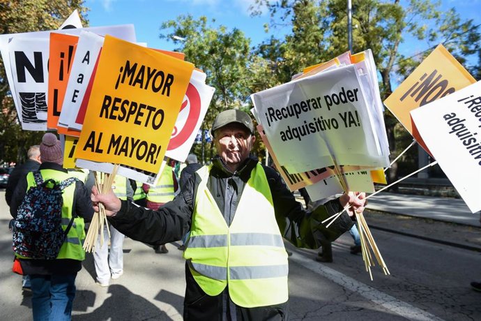 Un hombre sujeta varias pancartas en una manifestación de pensionistas