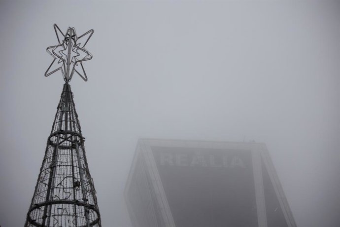 Un árbol de Navidad al lado de una de las 'Torres KIO' cubierta de niebla