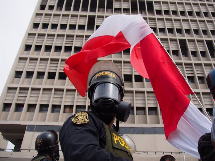 07 December 2022, Peru, Lima: A riot police officer with a gas mask stands under a Peruvian flag during a protest to celebrate the removal of President Pedro Castillo by congress for 'moral incapacity' after attempting a failed coup that sought to shut 