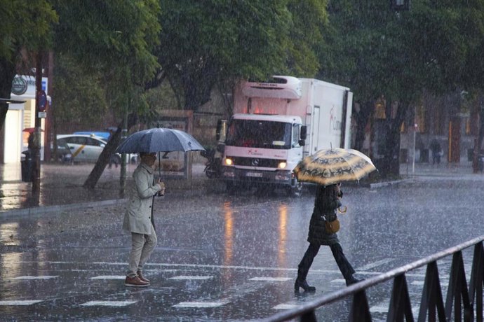 Dos mujeres cruzan bajo un paraguas un paso de peatones tras las fuertes lluvias en el puente del mes de diciembre en Sevilla