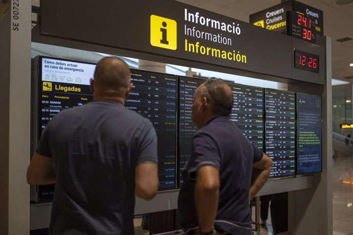 Archivo - Varias personas observan un panel de llegadas en el aeropuerto 