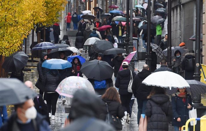 Personas caminan por la calle con paraguas.